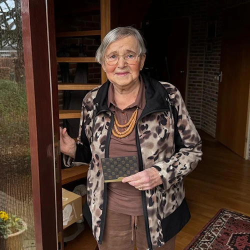 Mevrouw Kamphorst in de deuropening van haar woning, met in haar hand de gewonnen VVV-cadeaukaart