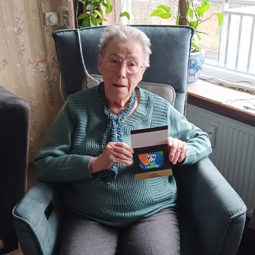 Mevrouw Molenaar in haar fauteuil, met een VVV-cadeaukaart in haar hand