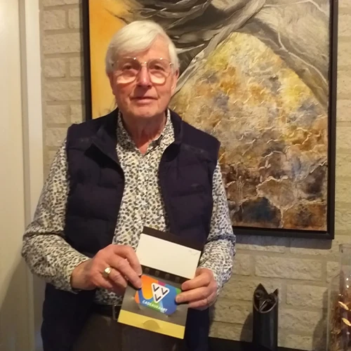 Meneer Zegers in de deuropening van zijn woning, met in zijn hand de gewonnen VVV-cadeaukaart