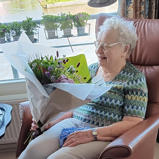 Mevr. Verduijn in haar stoel met een bos bloemen